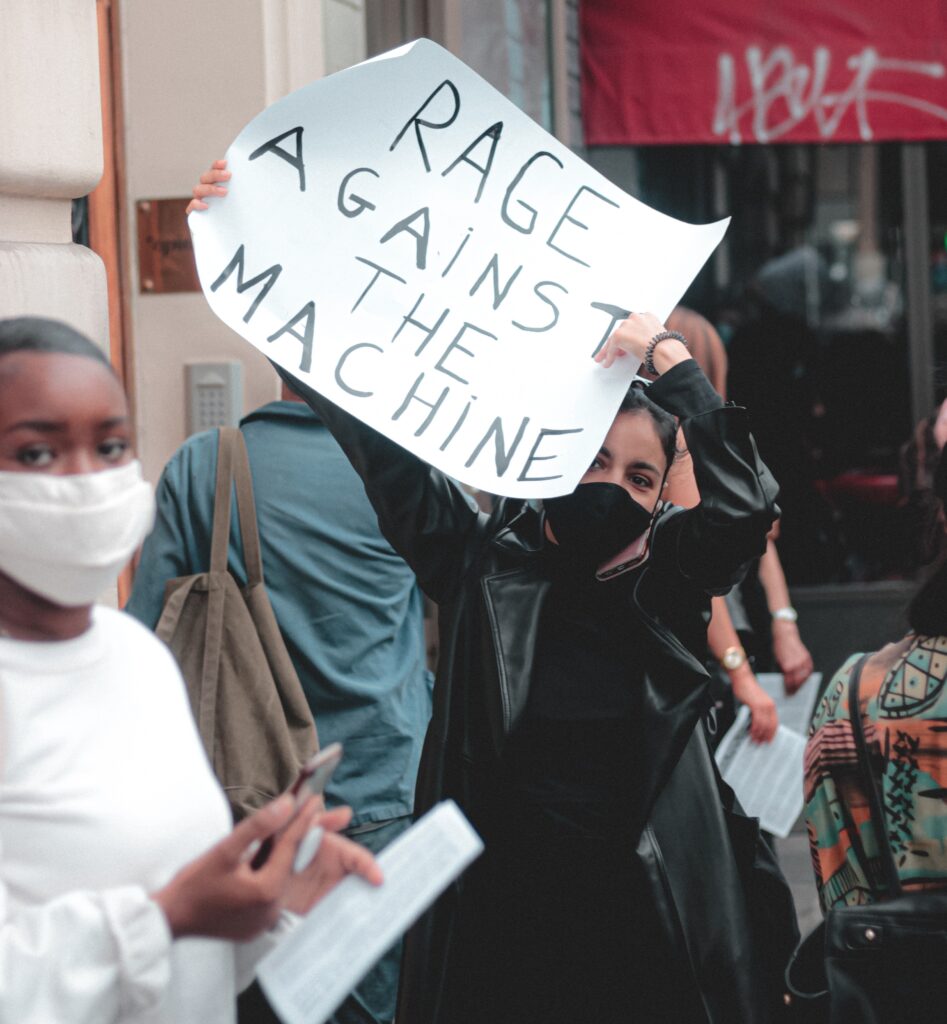 woman holding up a sign that reads "rage against the machine"
